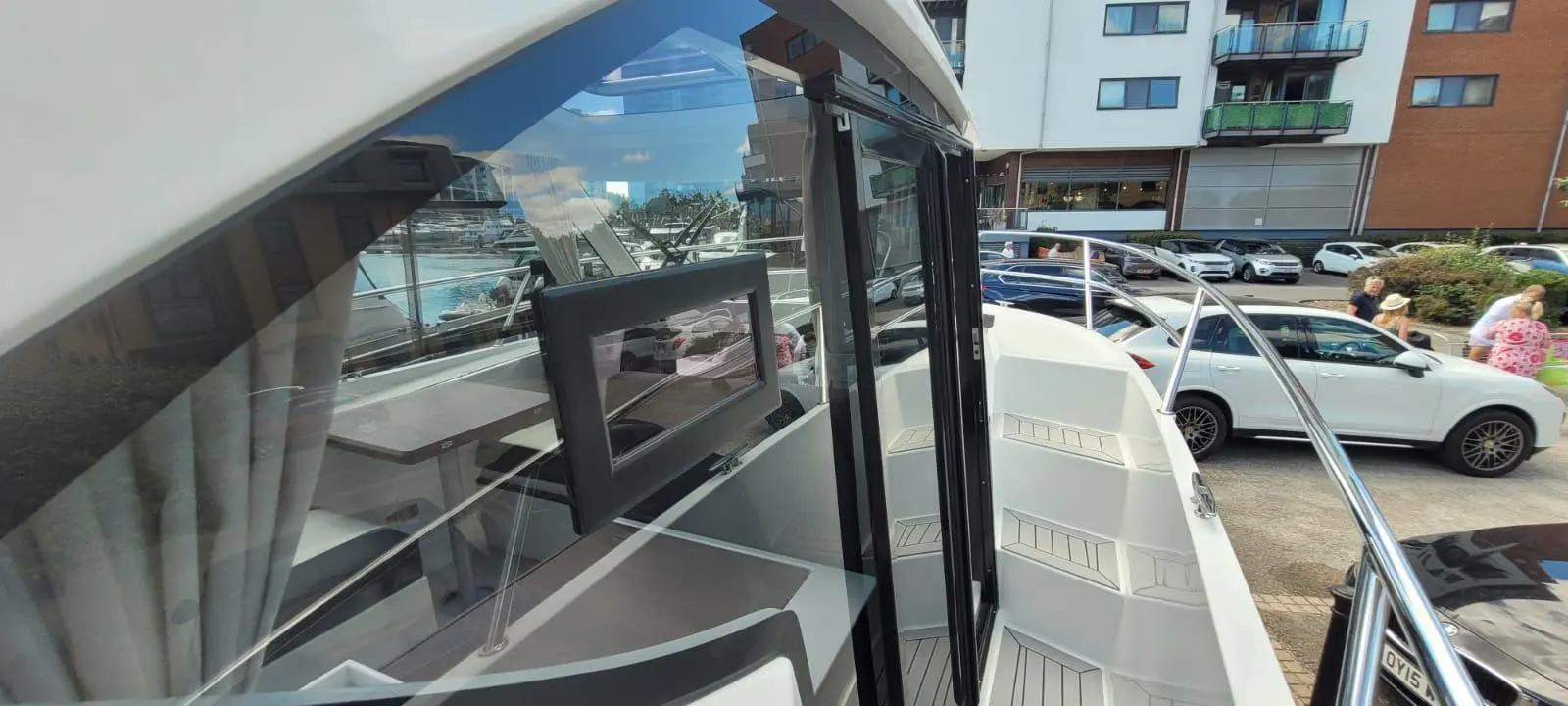 View of a modern boat interior with a boat window, seating area, and reflection of a marina visible outside.